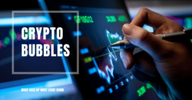 A hand holding a pen points to a “CRYPTO BUBBLES” graph on a screen, illustrating market volatility with the phrase “WHAT GOES UP MUST COME DOWN.