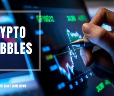 A hand holding a pen points to a “CRYPTO BUBBLES” graph on a screen, illustrating market volatility with the phrase “WHAT GOES UP MUST COME DOWN.