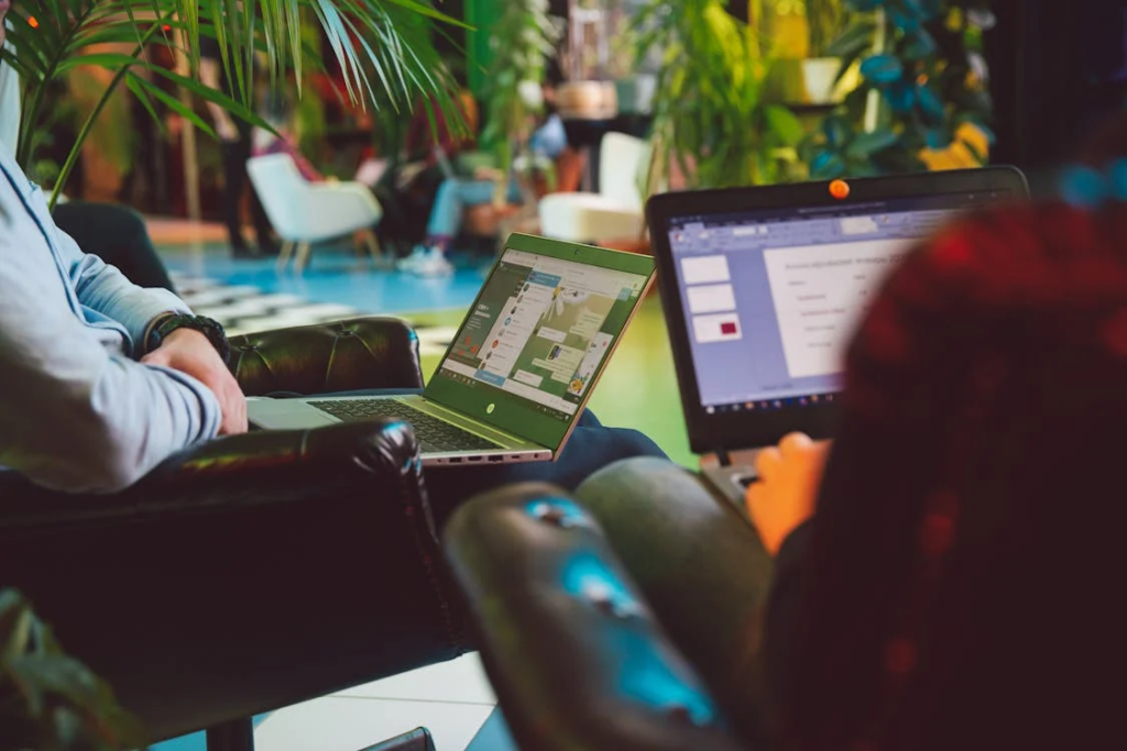 wo individuals seated in a modern workspace with laptops open on their laps, engaged in work, with one laptop displaying an SSL certificate error message.