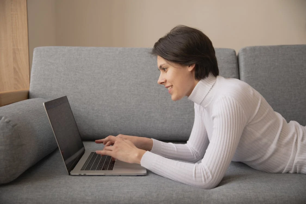 A person lying on a grey couch while using a laptop, symbolizing the everyday user’s need for an SSL Certificate to ensure secure online interactions.