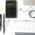 supply chain management . A flat lay image of a calculator, pen, pencil, magnifying glass, and financial documents with stock market data and a world map.