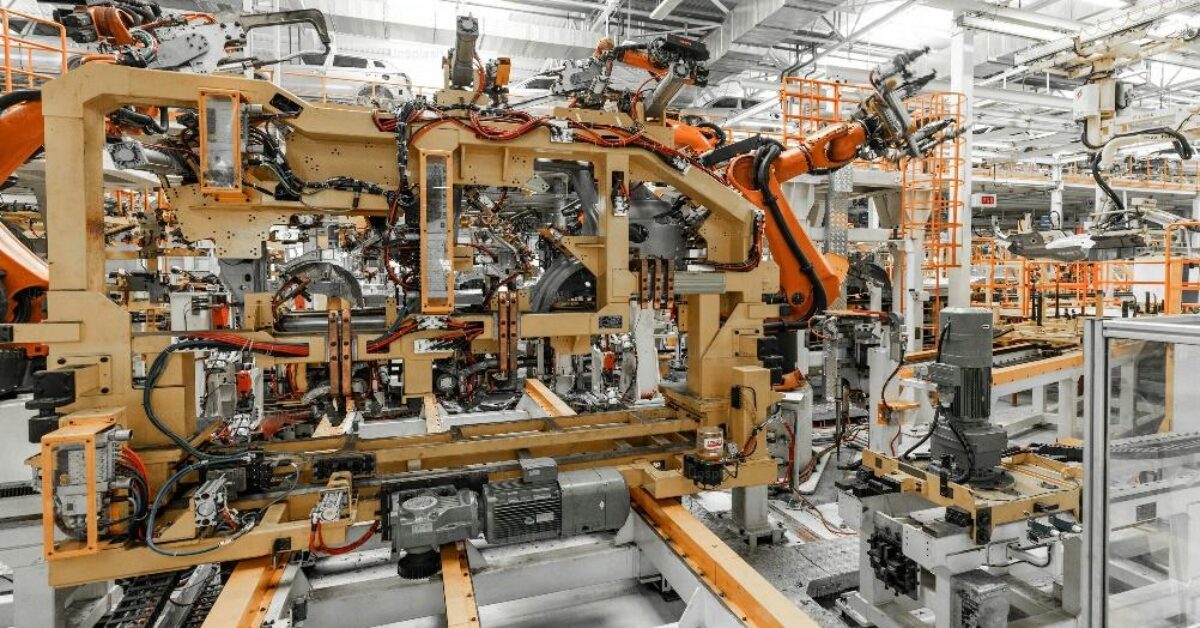 A large automation industrial factory with robotic arms automating the assembly of a car frame on an assembly line.